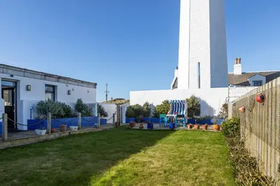 a yard in front of a white building with a lighthouse at Finest Retreats - Walney Island Lighthouse in Rampside