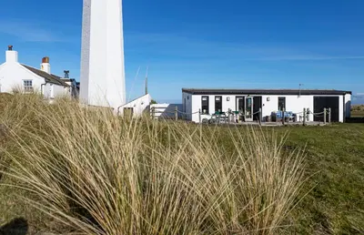 a white house with a lighthouse in the background at Finest Retreats - Walney Island Lighthouse in Rampside