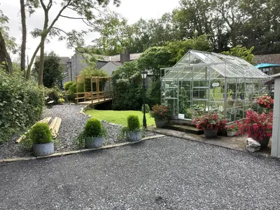 a greenhouse in a garden with potted plants at Lile Cottage at Gleaston Water Mill in Ulverston