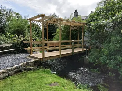 a wooden gazebo with a bridge over a river at Lile Cottage at Gleaston Water Mill in Ulverston