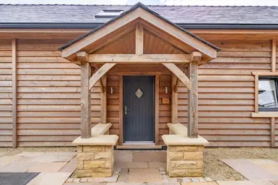 a wooden cabin with a black door and stone steps at Valley View Lodge Sleeps 8 with Hot Tub in Preston