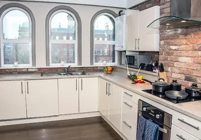 a kitchen with white cabinets and a brick wall at Base Serviced Apartments - Sir Thomas Street in Liverpool