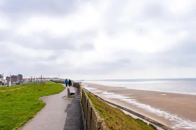 a person walking a dog on a sidewalk next to the beach at Families Only - Pet Friendly sleeps 6 maximum NO PARTIES in Blackpool