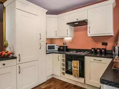 a kitchen with white cabinets and black counter tops at Mount Pleasant Cottage in Grange Over Sands