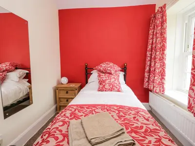 a red bedroom with a bed and a window at Mount Pleasant Cottage in Grange Over Sands