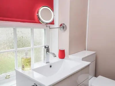 a bathroom with a white sink and a red window at Mount Pleasant Cottage in Grange Over Sands