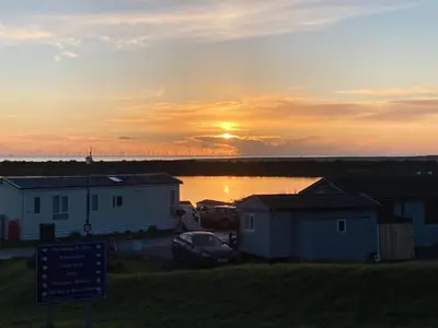a sunset over a body of water with houses and a sign at KINGDOM HOLIDAY PARK in Haverigg