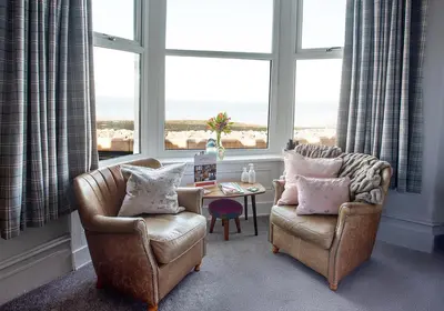 a living room with two chairs and a table and windows at The Broadwater Guest House in Morecambe