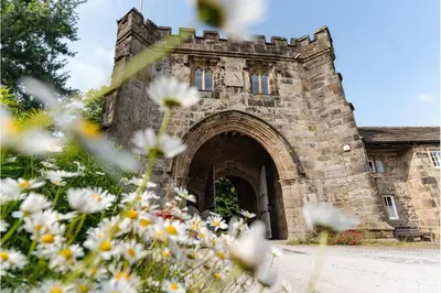 an old stone building with an archway in a field of flowers at Whalley Abbey - B&B and Retreat House in Whalley