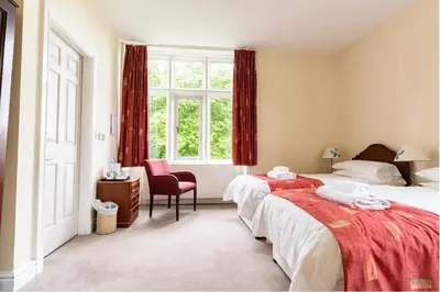 a bedroom with two beds and a chair and a window at Whalley Abbey - B&B and Retreat House in Whalley