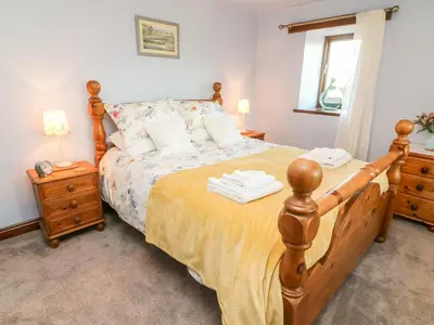 a bedroom with a wooden bed with a yellow bedspread at 1 Netherbeck Barn in Carnforth