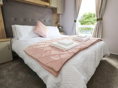 a bedroom with a pink and white bed with a window at 25 Sherwood in Carnforth