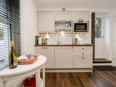 a kitchen with white cabinets and a table with a bottle of wine at Moorhurst Cottage in Grange Over Sands