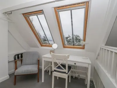 a attic room with a desk and two windows at Moorhurst Cottage in Grange Over Sands