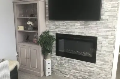a living room with a stone fireplace with a flat screen tv at Leafy Lytham central Lovely ground floor 1 bedroom apartment with private garden In Lytham dog friendly in Lytham St Annes
