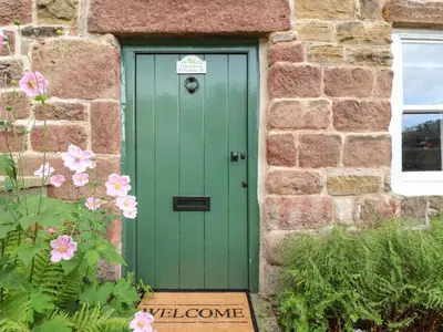 a green door in a brick building with pink flowers at Duckdown in Clitheroe