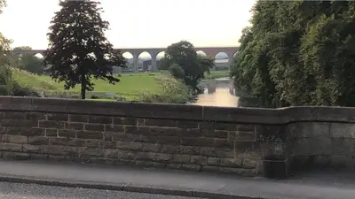 a brick retaining wall with a bridge in the background at Riverside Cottage in Whalley
