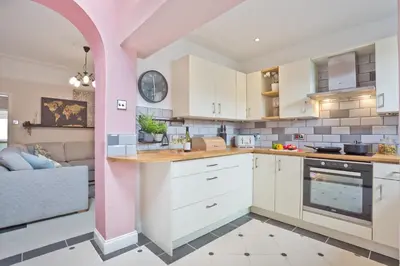 a kitchen with white cabinets and a pink wall at Malleus House in Barrow in Furness