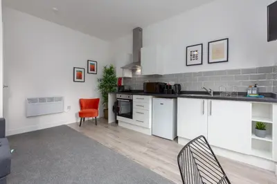 a kitchen with white cabinets and red chairs at Charles Alexander Short Stay - Charnley House Apartments in Blackpool