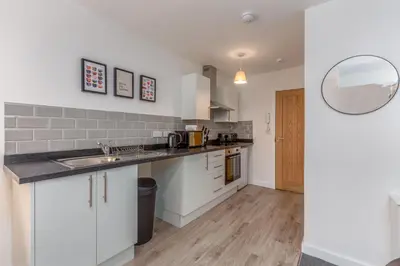 a kitchen with white cabinets and a sink and a mirror at Charles Alexander Short Stay - Charnley House Apartments in Blackpool