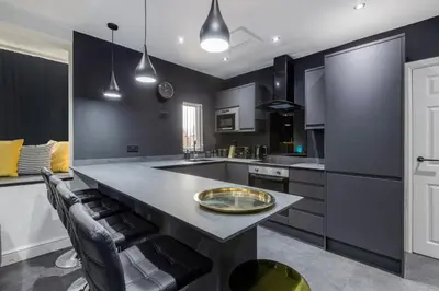 a kitchen with black cabinets and a large island with a table at TWO BED Modern Apartment 5min walk to Town centre with Free Parking ! Under New Management in Blackpool