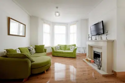 a living room with two green couches and a fireplace at Contractors and Pets Welcome, Only 2 miles from M57, M58, Whole House Rental Sleeps 4 to 9, Short Walk to Orrell Station in Liverpool