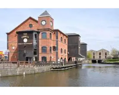 a large brick building with a clock tower next to a river at Central Wigan welcoming Townhouse sleeps up to 6 in Wigan