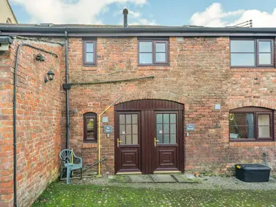 a brick house with a wooden door and two windows at The Barn in Poulton le Fylde