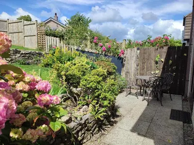 a garden with a fence and a table and flowers at Gorgeous Cottage near Cartmel with FREE SPA Access in Holker