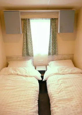 two beds in a small room with a window at Plot 8 Lakeside Cabin, Wyldecrest, Millom in Millom