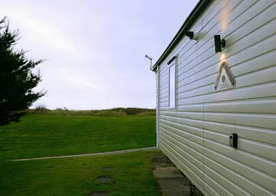 a side of a white building with a field behind it at Plot 8 Lakeside Cabin, Wyldecrest, Millom in Millom