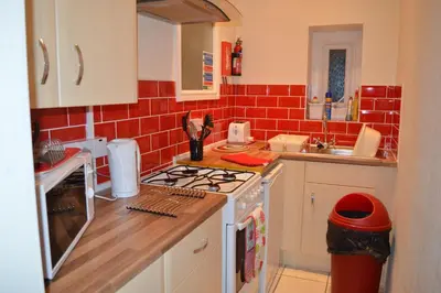 a kitchen with a stove and a red tile wall at Ayrton House Holiday Apartments in Blackpool