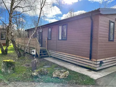 a small red cabin with a porch and a tree at Coniston View 7 in Warton