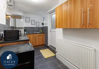 a kitchen with wooden cabinets and a black refrigerator at FLATZY - Modern Apartment Close to Football Stadiums in Liverpool