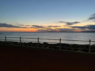 a sunset over a body of water with a fence at Eden Vale Garden View Apartment with Patio in Morecambe