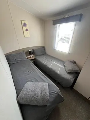 two beds in a small bedroom with a window at 3 Bedroom Modern Caravan Sleeps up to 8 in Millom