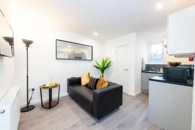a living room with a black couch and a kitchen at The Blossoms Studio Apartments in Liverpool