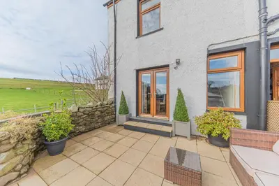 a house with a patio and a stone wall at The Black Dog Cottage in Dalton in Furness
