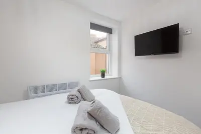 a white bedroom with towels on a bed with a flat screen tv at Charles Alexander Short Stay - The Gateway in Blackpool