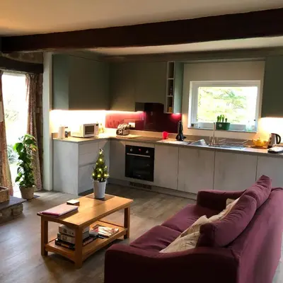a living room with a purple couch and a kitchen at Locka Old Hall Cottage in Arkholme
