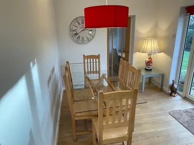 a dining room with a table and chairs and a clock at 'Sounion' - Fabulous, spacious modern house with large private garden in Leafy Lytham in Lytham St Annes