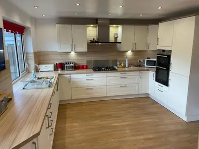 a kitchen with white cabinets and wooden floors at 'Sounion' - Fabulous, spacious modern house with large private garden in Leafy Lytham in Lytham St Annes