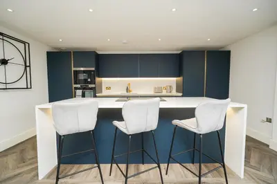 a kitchen with a white counter and three stools at NOVU Apartments Duke Street Liverpool in Liverpool