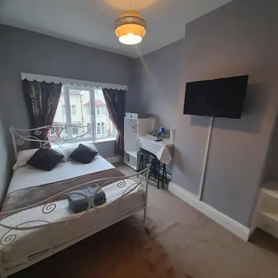a bedroom with a bed with a tv on the wall at Merginn Guest House in Blackpool