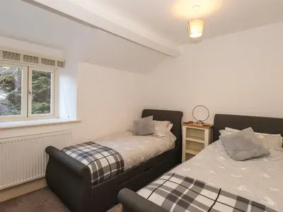 a bedroom with two beds and a chair in it at 1 The Stables in Grange Over Sands