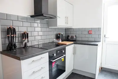 a kitchen with white cabinets and black counter tops at Withnell Stays - Apartment One - Ground Floor - Retro Gaming Machine in Blackpool