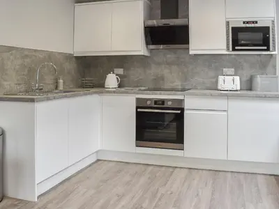 a kitchen with white cabinets and a sink and a stove at Woodgate Cottage in Dalton in Furness