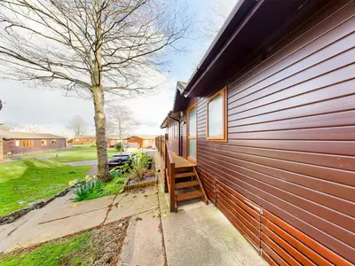 a house with a wooden staircase next to a building at 3 Bedroom Lakeview Lodge - Ensuite & Balcony Deck in Carnforth