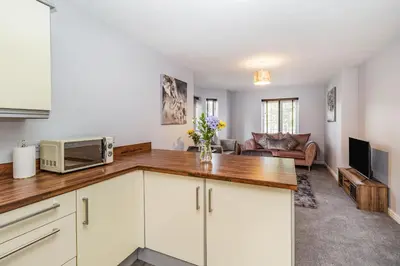 a kitchen with white cabinets and a living room at Mayfair in Wigan