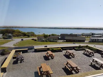 a patio with picnic tables and a view of the water at Herdwicks in Millom